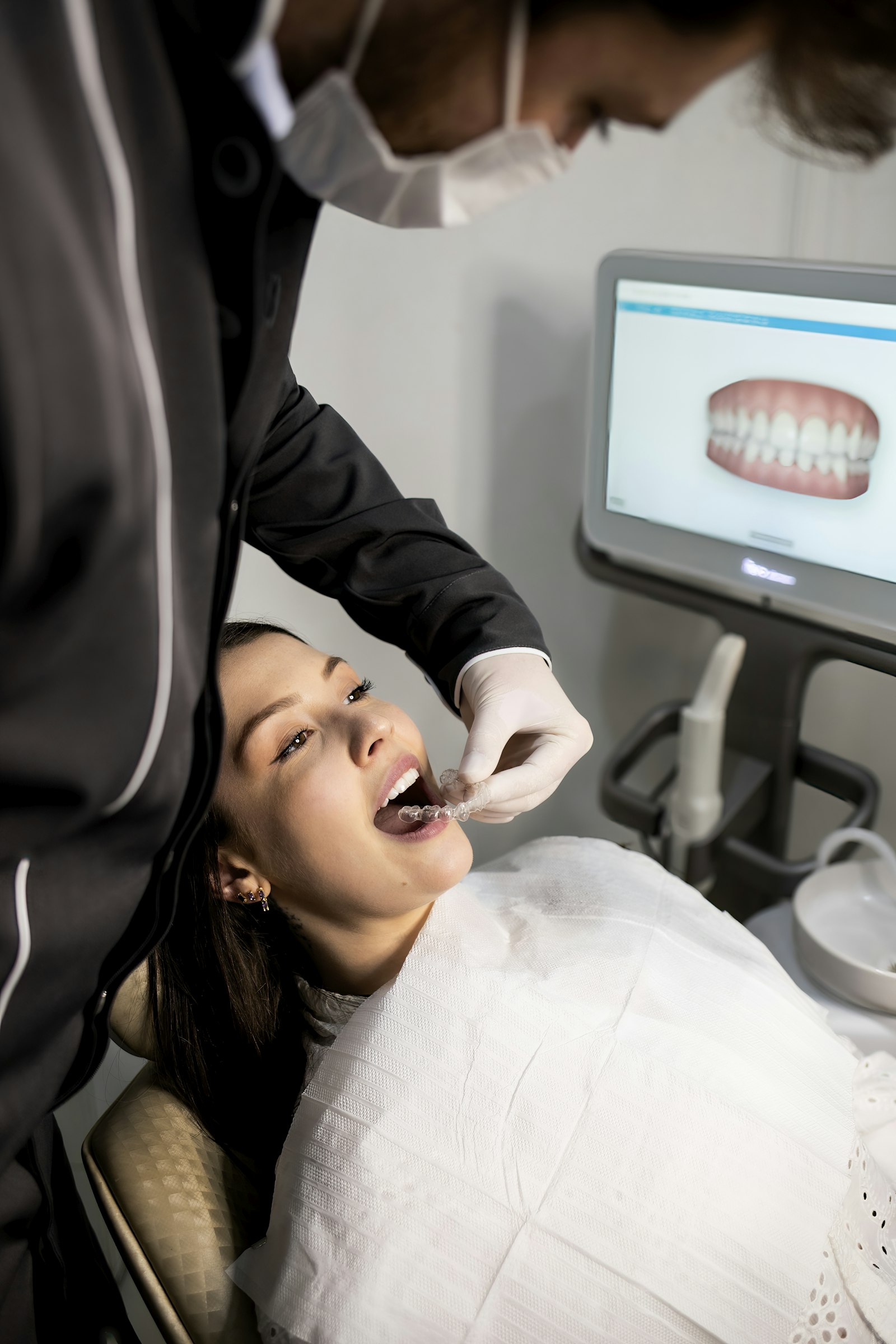 Dentist fitting a clear aligner while a digital 3D scan of the patient's teeth shows on screen